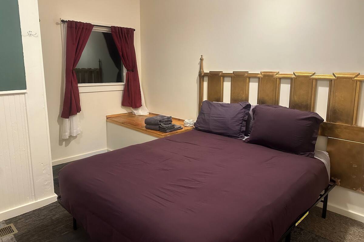 Une chambre à coucher avec un lit, une table de chevet, une fenêtre avec des rideaux et un radiateur.