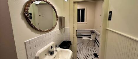 Un baño estrecho con un lavamanos blanco, un espejo y un inodoro.