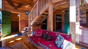 A wooden cabin interior with a staircase, a red sofa with patterned cushions, and a green door. - 44mbr - Hot Tub- Pets Ok - Wifi - Bbq - Sleeps 8 2 Bedroom Home by RedAwning (Deming)