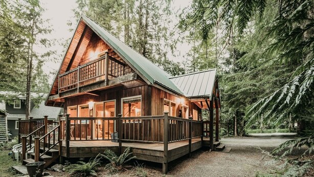A two-story log cabin with a balcony, surrounded by dense forest. - 32mbr - Bbq - Pets Ok - Wood Stove - Sleeps 7 3 Bedroom Home by RedAwning (Deming)