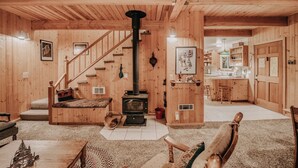 A cozy wooden interior with a staircase, a fireplace, a kitchen area, and a living room with a sofa and a coffee table. - 32mbr - Bbq - Pets Ok - Wood Stove - Sleeps 7 3 Bedroom Home by RedAwning (Deming)