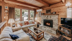 Ein gemütliches Blockhaus-Interieur mit Kamin aus Stein, Holzwänden, einer Couch, einem Couchtisch und einem Bücherregal.