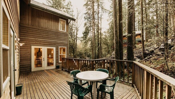 A wooden deck with a round table and chairs, surrounded by tall trees.