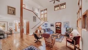 A spacious living room with a wooden floor, a staircase, a blue sofa, a wooden coffee table, and a television.