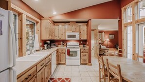 A compact kitchen with wooden cabinets, a microwave, stove, and a dining area with a table and chairs. - 34sl - Hot Tub - Bbq - Ping Pong Table - Sleeps 8 3 Bedroom Home by RedAwning (Deming)