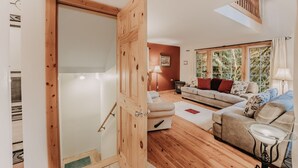 A wooden door leading to a living room with a sofa, a lamp, and a view of trees through large windows. - 34sl - Hot Tub - Bbq - Ping Pong Table - Sleeps 8 3 Bedroom Home by RedAwning (Deming)