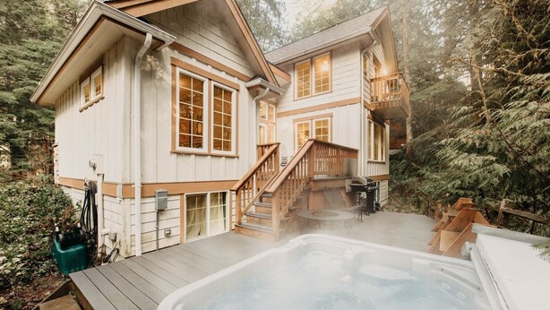 A two-story house with a hot tub on the deck, surrounded by trees. - 34sl - Hot Tub - Bbq - Ping Pong Table - Sleeps 8 3 Bedroom Home by RedAwning (Deming)