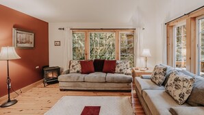 A cozy living room with a fireplace, two sofas, and large windows offering a view of trees. - 34sl - Hot Tub - Bbq - Ping Pong Table - Sleeps 8 3 Bedroom Home by RedAwning (Deming)