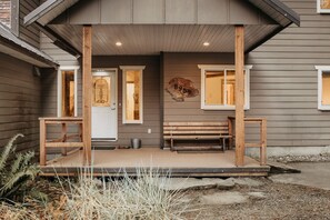 Enter a charming home with a covered porch, featuring a bench and two doors, one with a decorative glass panel.