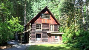 A rustic log cabin with a steep gabled roof, a front porch, and a gravel driveway leading to the entrance. - 31sw - Fireplace - Wifi - Washer/dryer - Sleeps 4 2 Bedroom Home by RedAwning (Deming)