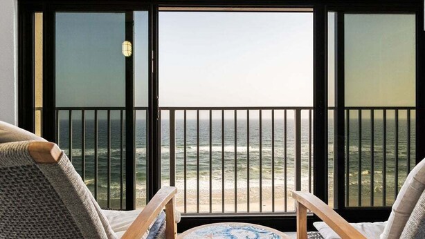 A balcony with a view of the ocean, featuring two wooden chairs and a small round table.