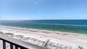 A beach view with a clear sky, sandy beach, and a wooden walkway leading to beach umbrellas.