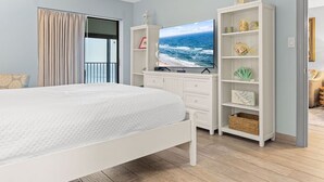 A bedroom with a bed, a TV, a wardrobe, and a view of the ocean.