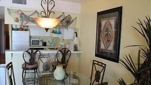 A dining area with a round glass table, four chairs, a vase, and a decorative wall piece.