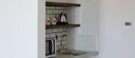 A compact kitchen with white walls, a wooden floor, a dishwasher, a sink, and a kettle on the countertop.