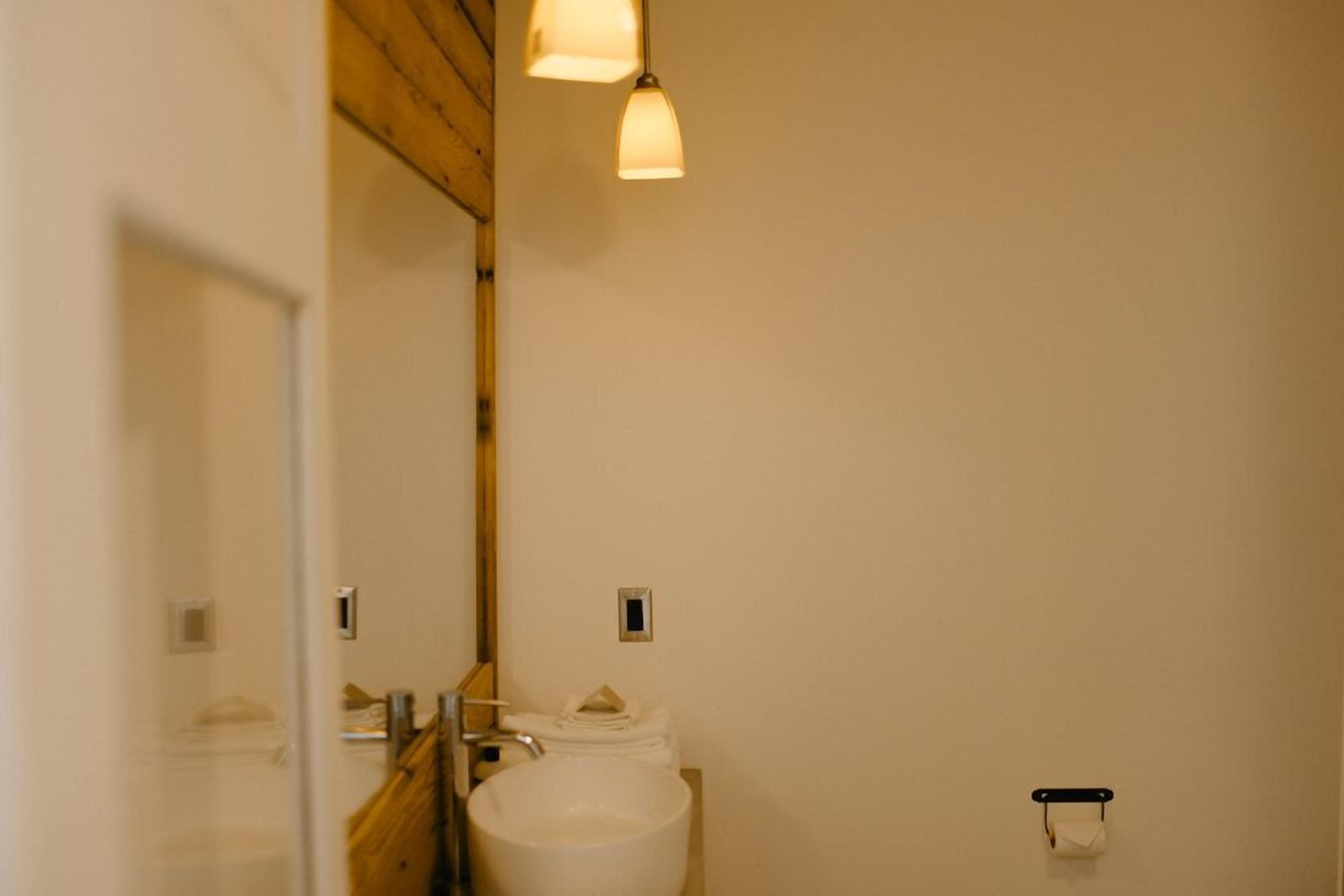 A bathroom with a white sink, a mirror, and a toilet. There are two light fixtures above the sink.