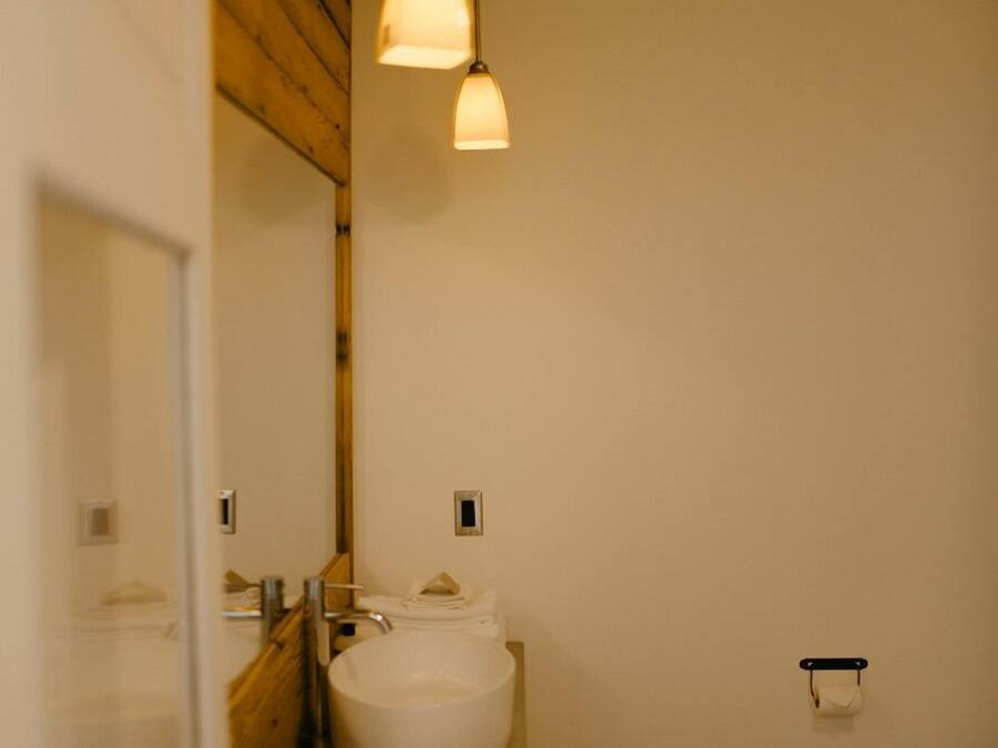 A bathroom with a white sink, a mirror, and a toilet. There are two light fixtures above the sink.