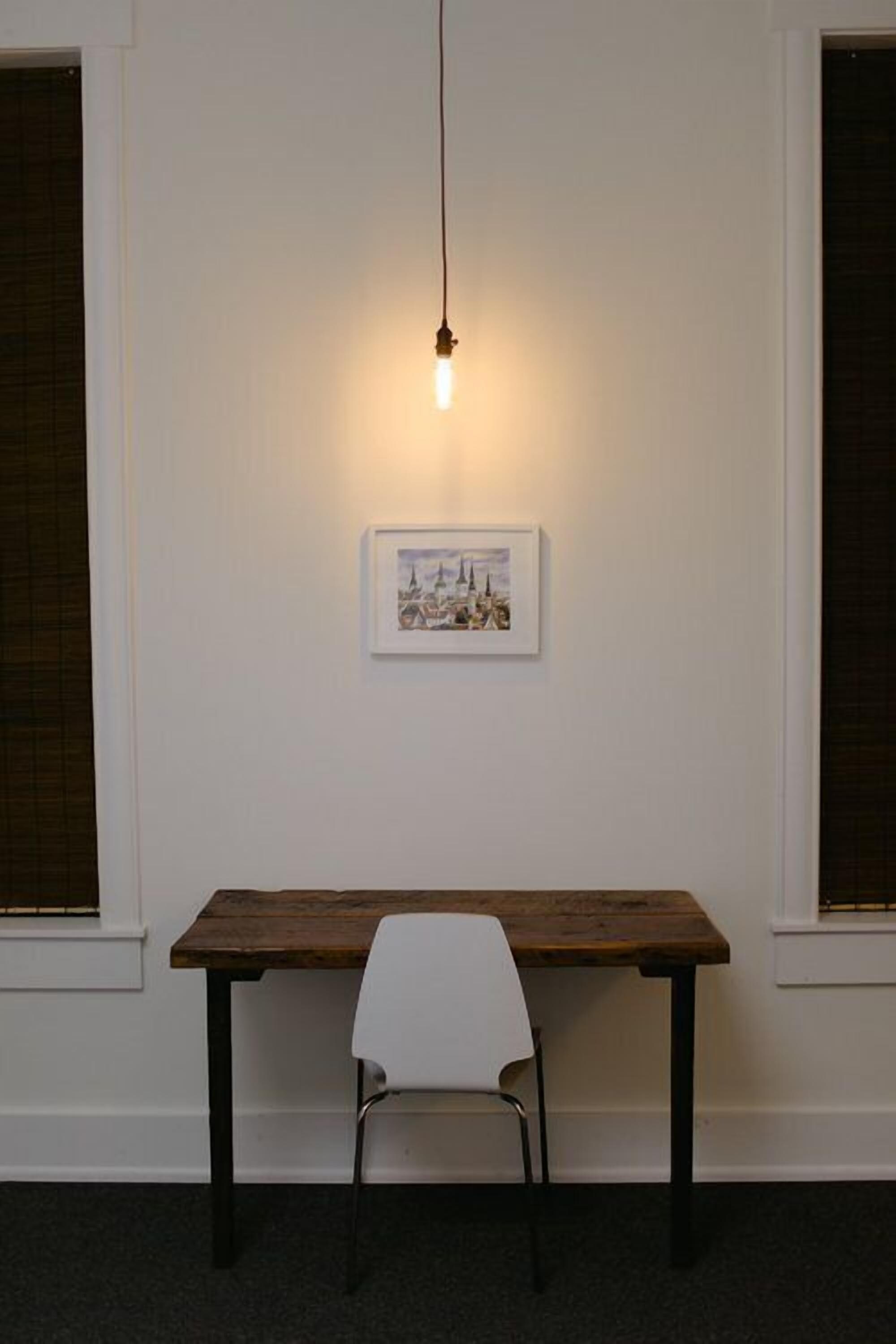 A room with a wooden table and a white chair, a hanging light fixture, and a framed picture on the wall.