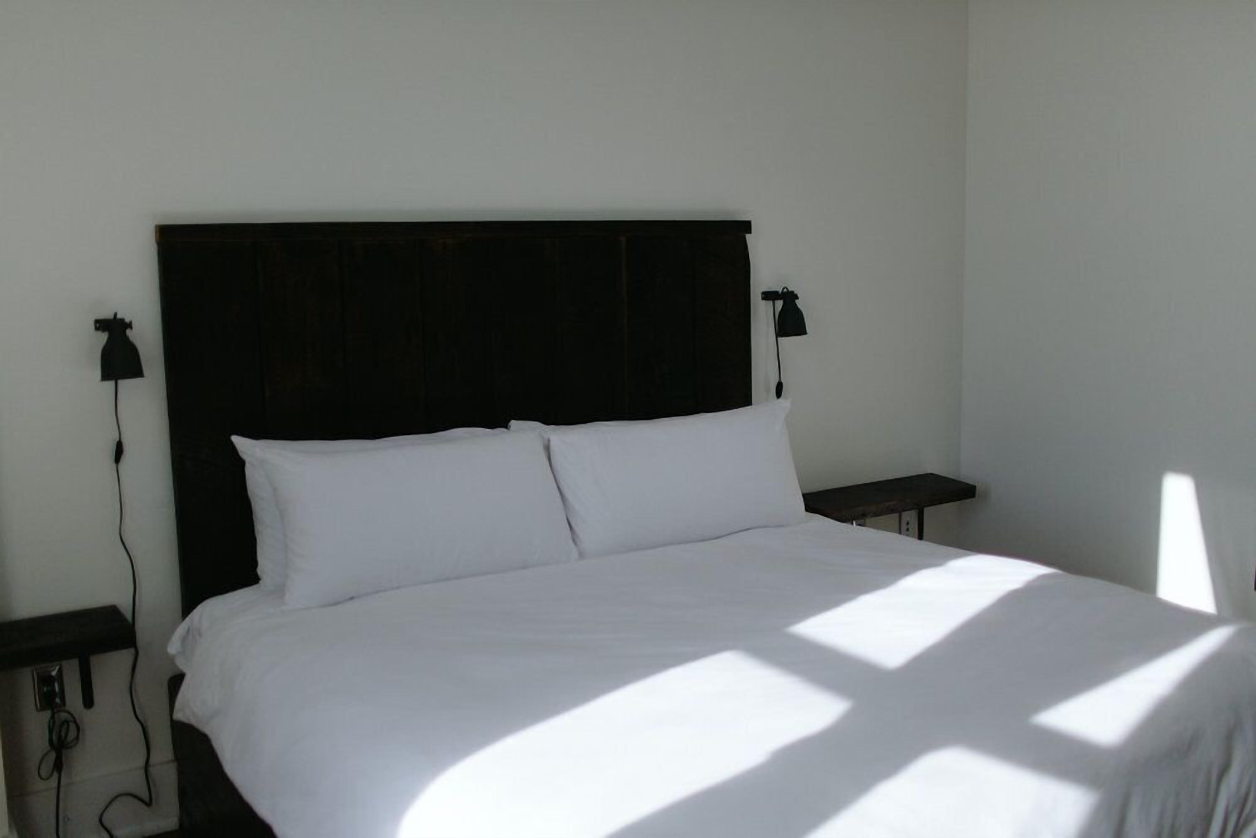 A bed with white linens, a dark headboard, and two bedside lamps.