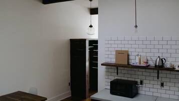 A compact kitchen with white tiled backsplash, a microwave, a wooden table, and a hanging light fixture.