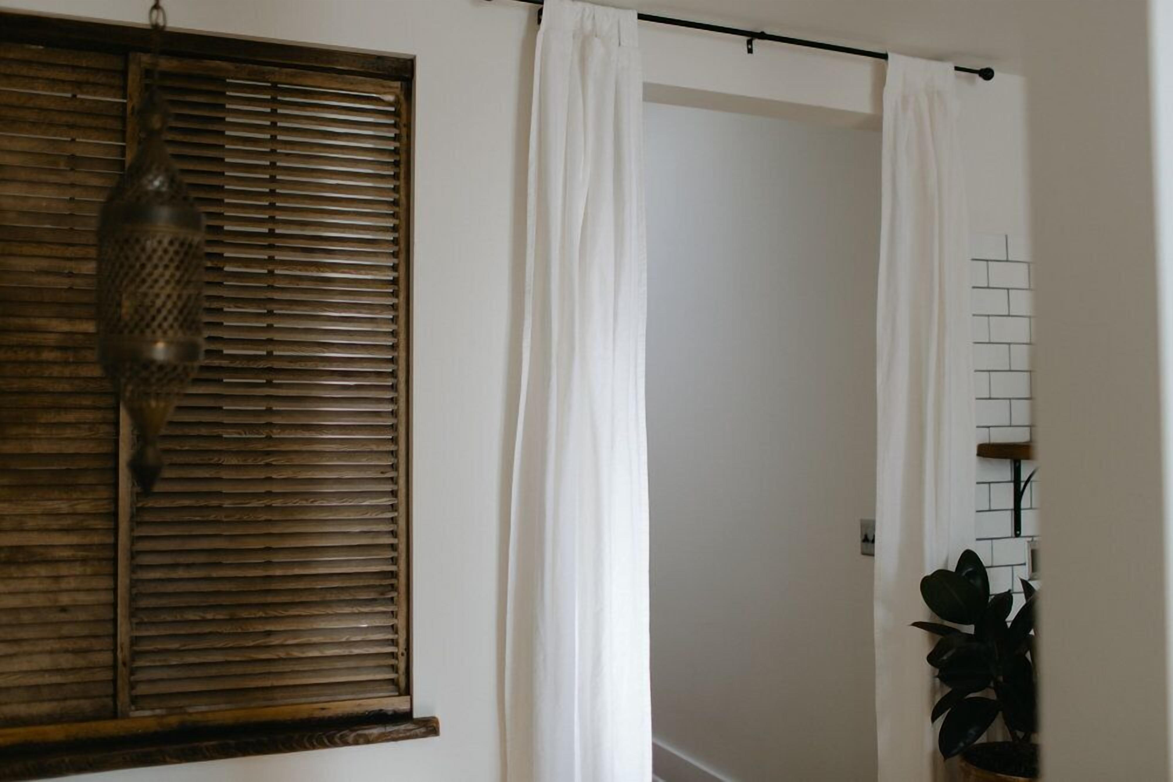 Um quarto com janela de madeira, cortinas brancas e parede revestida de azulejos.