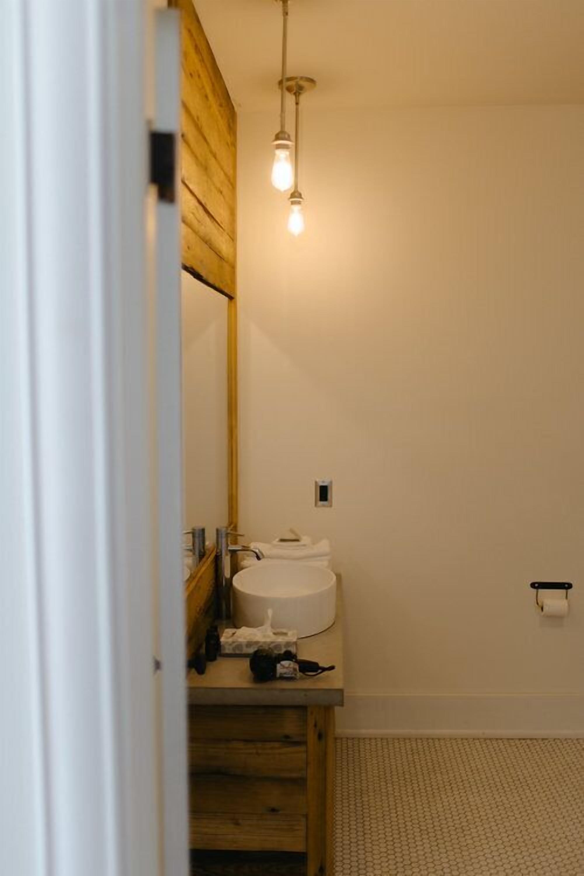 Un baño con tocador de madera, lavamanos blanco y lámpara colgante.