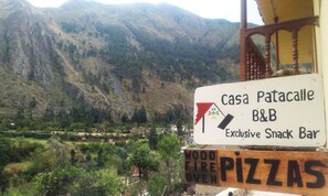 A sign for Casa Patacalle B&B, an exclusive snack bar, with a view of mountains in the background. - Casa Patacalle Bed & Breakfast Hotel (Ollantaytambo)