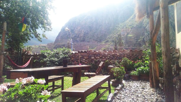 An outdoor seating area with wooden tables and chairs, surrounded by lush greenery and a stone wall. - Casa Patacalle Bed & Breakfast Hotel (Ollantaytambo)