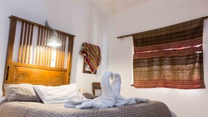 A bed with patterned bedding, a wooden headboard, a hanging quilt, and a window with a striped curtain. - Casa Patacalle Bed & Breakfast Hotel (Ollantaytambo)