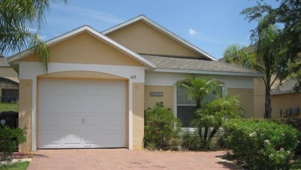 A single-story house with a white garage door, beige exterior walls, and a sloped roof. - Beautiful Vacation Home fully equipped (Haines City)