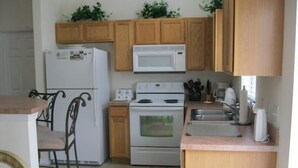 A compact kitchen with wooden cabinets, a white refrigerator, a microwave, a stove, and a sink. - Beautiful Vacation Home fully equipped (Haines City)