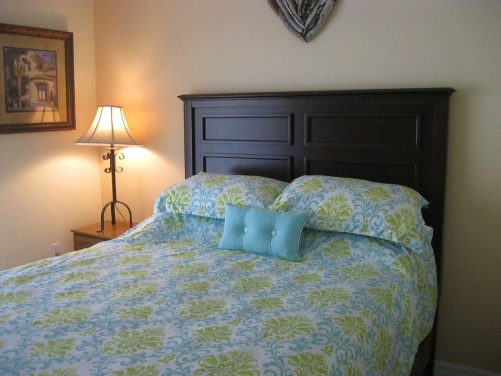 Un lit avec une couvre-lit à motifs, une tête de lit, une lampe de chevet et un tableau encadré accroché au mur.