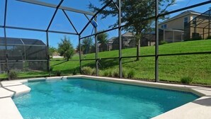 A swimming pool with a clear blue water, surrounded by a white deck and a glass enclosure. - Beautiful Vacation Home Especially Convenient (Haines City)
