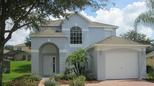 A two-story house with a garage, a front yard with a tree, and a brick driveway. - Beautiful Vacation Home Especially Convenient (Haines City)