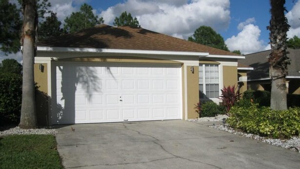 A single-story house with a white garage door, a beige exterior, and a sloped roof. - Beautiful Vacation Home Close by Theme Parks (Haines City)