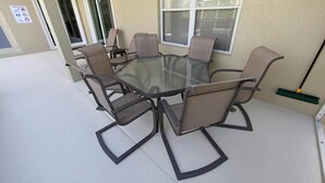 Une table ronde en verre, six chaises, un balai et une fenêtre avec des stores.