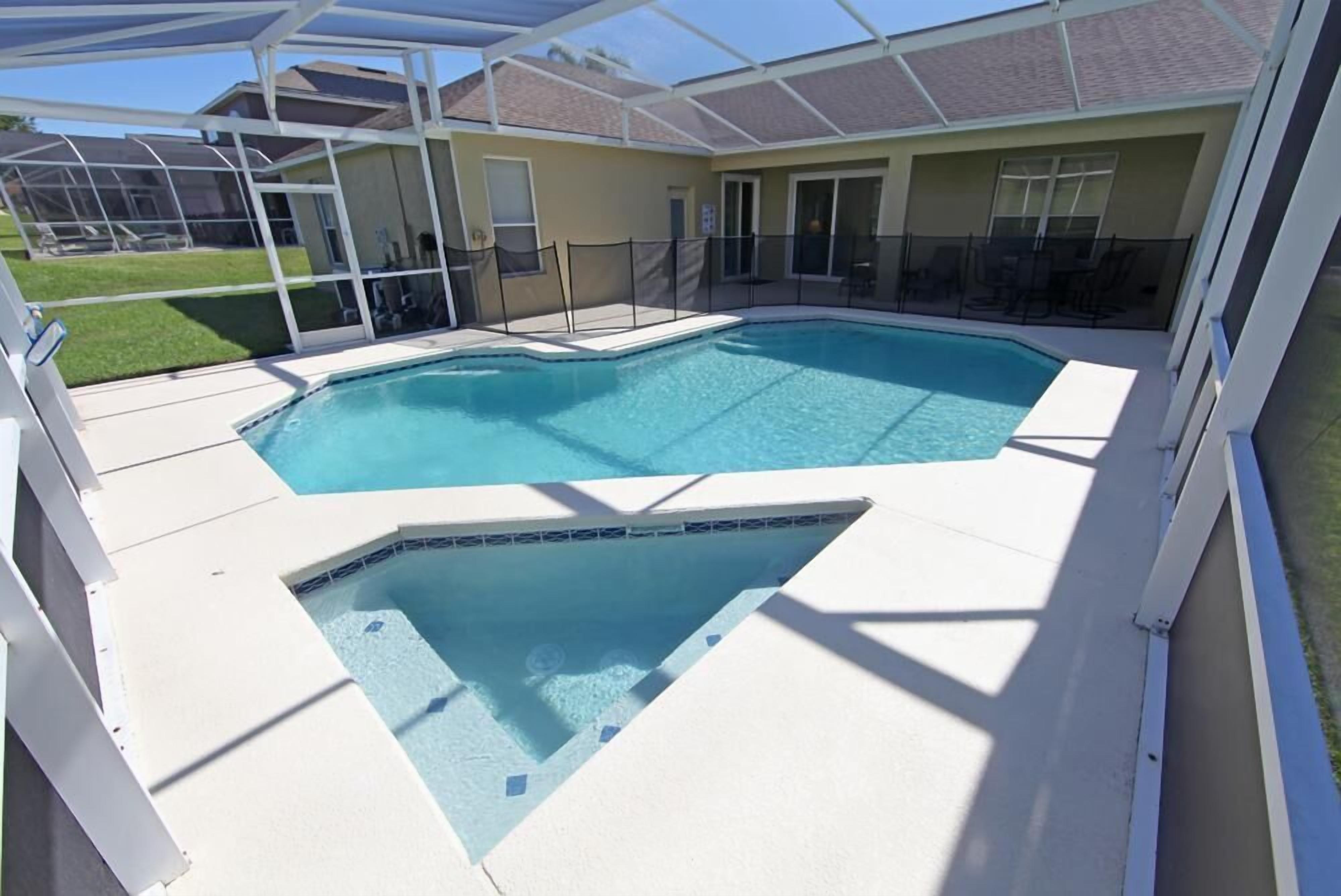 A swimming pool with a sunshade structure, surrounded by a fenced area and a grassy lawn.