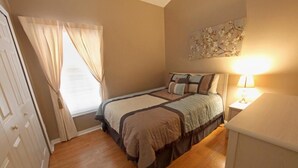 Ein Schlafzimmer mit einem Bett, einem Nachttisch, einer Lampe, einem Fenster mit Vorhängen und einer Tür.