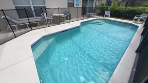 Ein Innenpool mit klarem, blauem Wasser, umgeben von einem schwarzen Schutzzaun, neben einem Gebäude mit einer überdachten Terrasse.