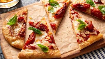 Pizza mit Tomaten und Basilikum auf einem Holzbrett.