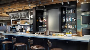A modern bar area with a long counter, bar stools, and shelves stocked with bottles.