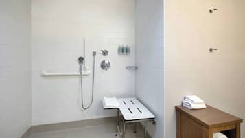 Un baño con paredes de azulejos blancos, una ducha con cabezal de mano, un perchero y un armario de madera con una toalla.