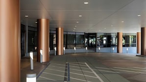 A spacious indoor area with large columns, a patterned floor, and glass doors leading outside.