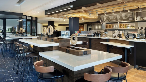 A modern bar area with multiple seating options, including bar stools and high tables, and a visible kitchen area with bar equipment.