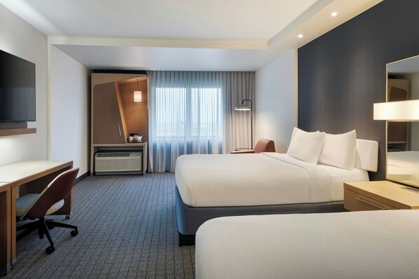 Una habitación de hotel con una cama grande, un escritorio, una silla, un televisor y un espejo.