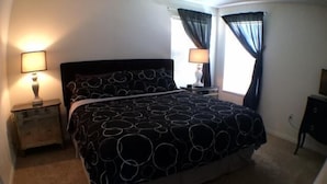 A bedroom with a bed, two bedside lamps, a nightstand, a dresser, and a window with curtains. - Lovely Home Perfect for a Family (Haines City)