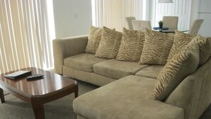 A living room with a beige sectional sofa, a wooden coffee table, and a lamp on a side table. - Lovely Home Perfect for a Family (Haines City)