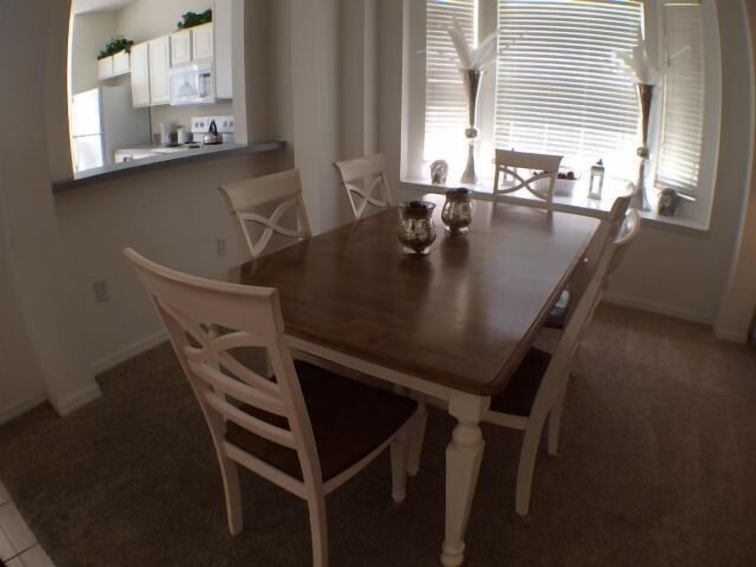 Un coin repas avec une table en bois et des chaises blanches. Deux vases décoratifs sont posés sur la table.