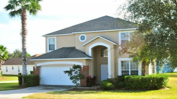 A two-story house with a garage, a small front porch, and a landscaped yard. - Lovely Home Perfect for a Family (Haines City)