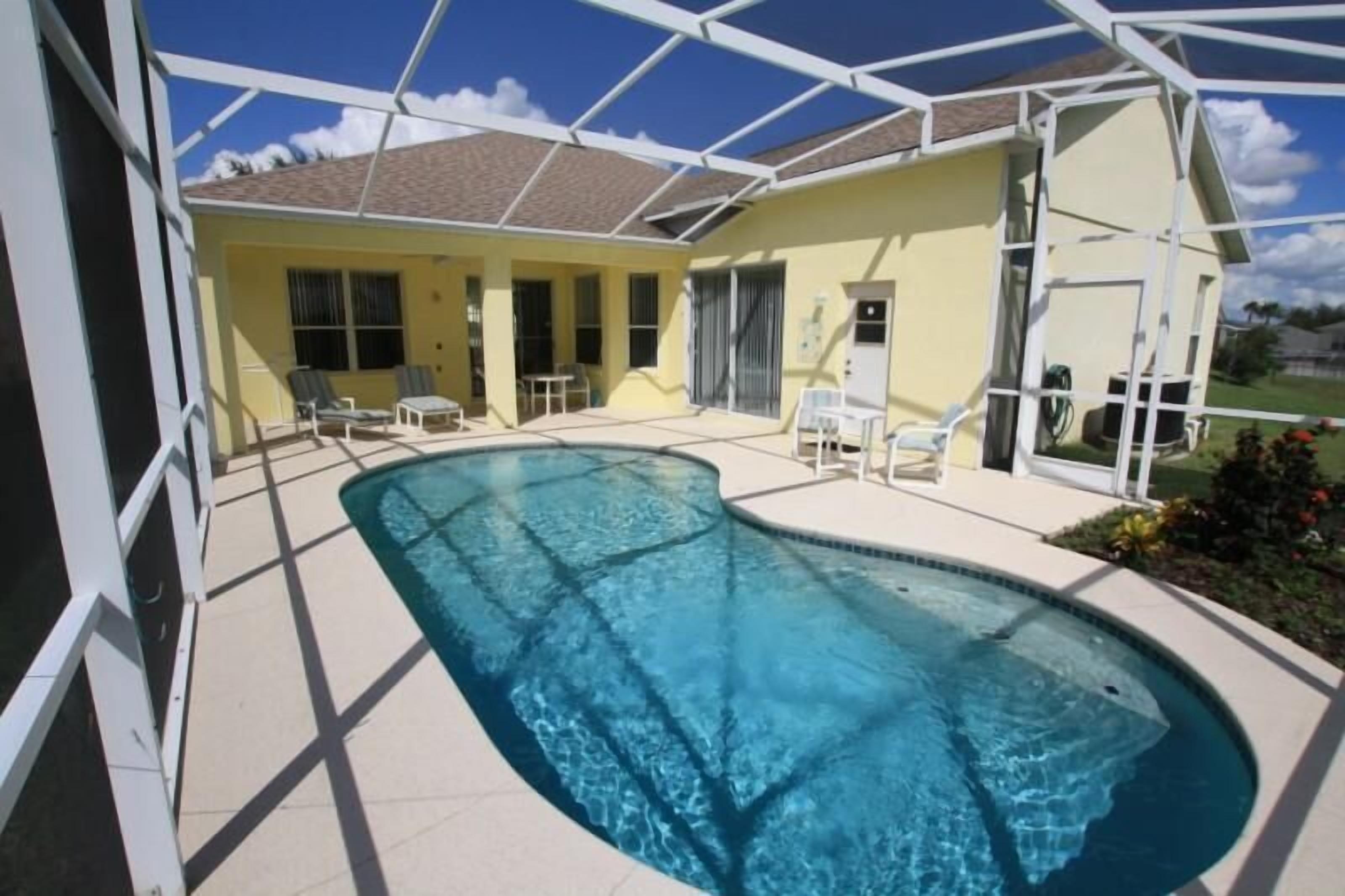 Ein Poolbereich mit klarem, blauem Pool, umgeben von einer überdachten Terrasse mit Stühlen und einem Tisch.